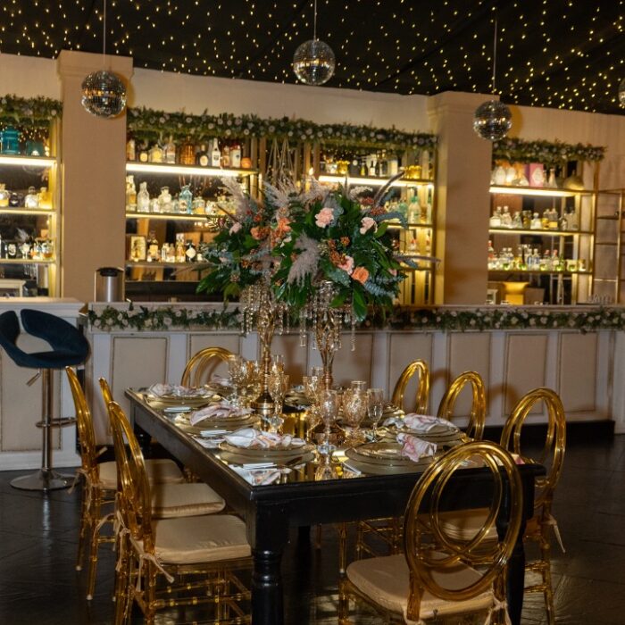 Detalle del mobiliario elegante y montaje de mesa en el Salón Gatsby de Amara Home, hacienda para bodas y eventos con barra y vitrinas de licor al fondo