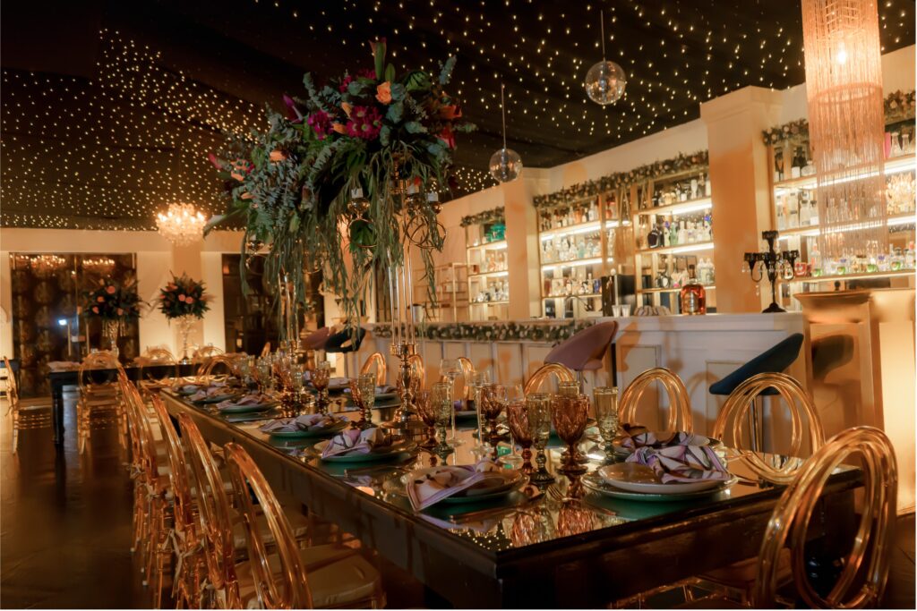 Mesa imperial con mobiliario elegante, centros de mesa y barra iluminada en el salón de Amara Home, hacienda para bodas y eventos